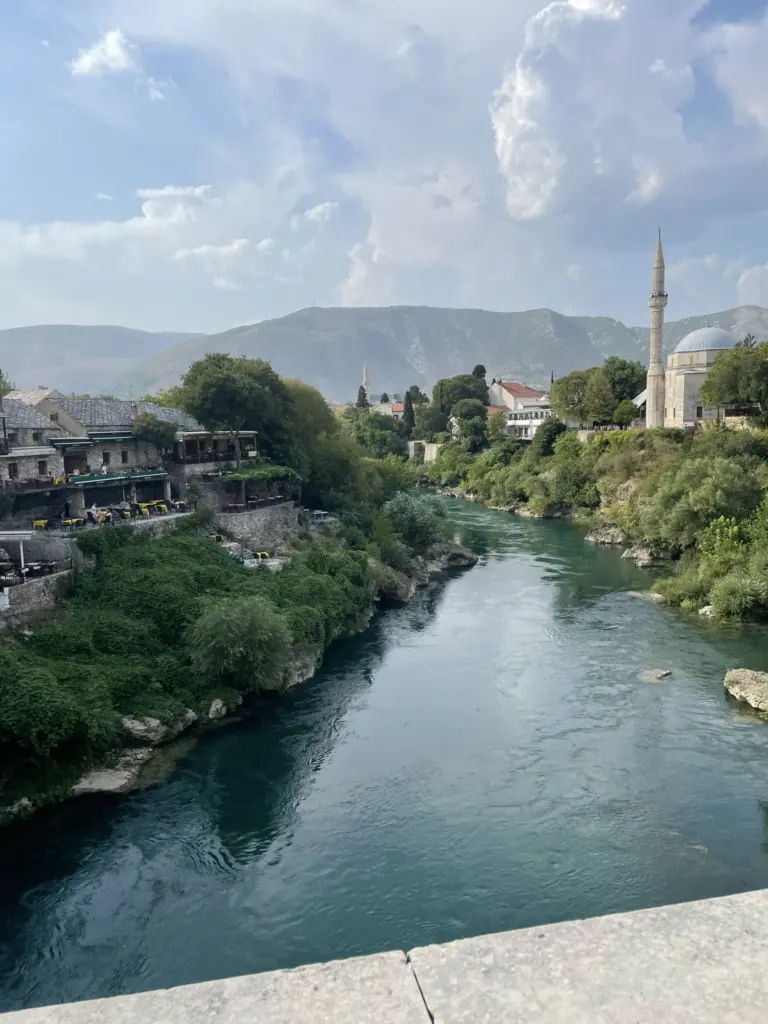 La Grande Mosquée de Mostar en Bosnie, avec son minaret élancé et son architecture ottomane traditionnelle, entourée de jardins et de visiteurs.