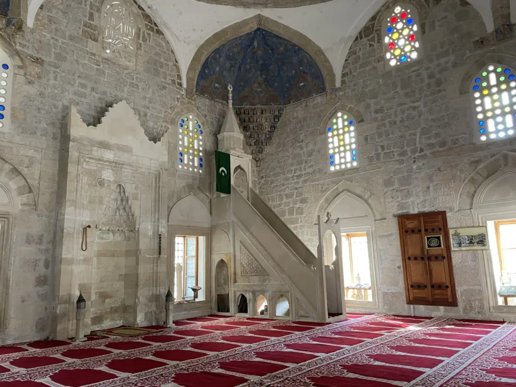 Intérieur de la Mosquée Hajji Alija à Počitelj avec décoration islamique traditionnelle et lumière naturelle.