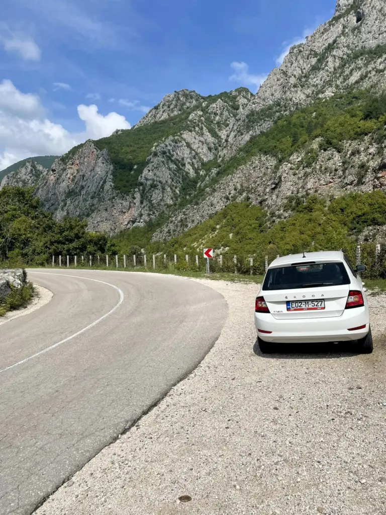 R_Une voiture est arrêtée sur le bas-côté de la route menant au parc naturel de Blidinje, entourée de paysages montagneux.