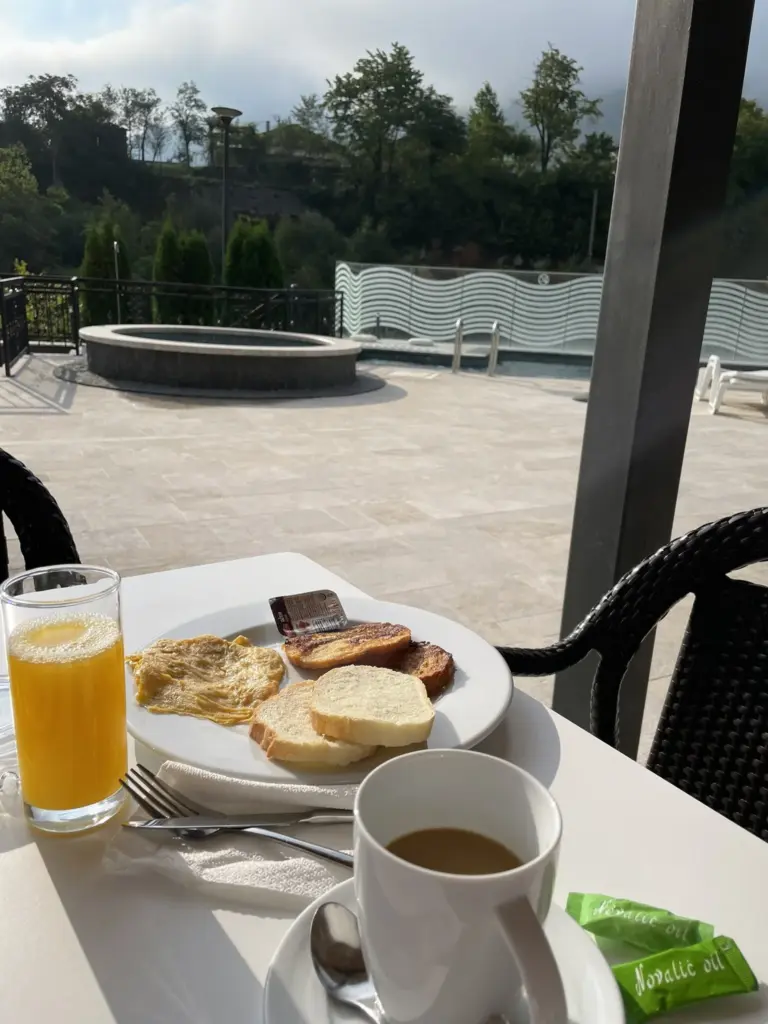 Petit déjeuner servi en terrasse d’un hôtel, avec vue sur les collines et lumière du matin.
