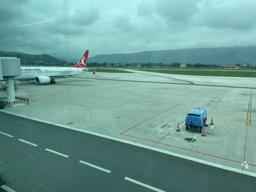Vue sur le tarmac de l’aéroport international de Sarajevo en Bosnie, avec des avions stationnés et les montagnes en arrière-plan.
