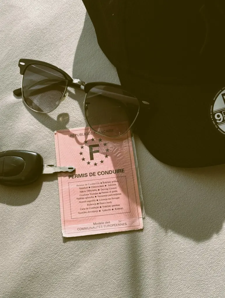Permis de conduire français posé sur une table à côté d’un trousseau de clés, d’une casquette et de lunettes de soleil.
