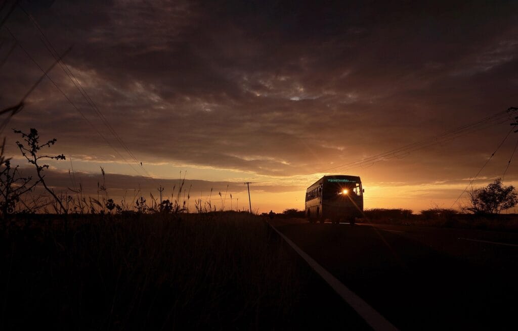 Un bus roule et est déplacer sur une route tranquille au lever du soleil, baigné par une lumière dorée et entouré de paysages calmes.