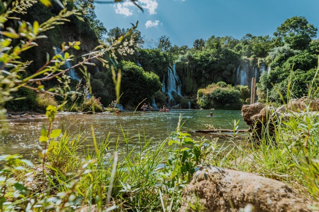 Vue des chutes de Kravica depuis le bord de l’eau, avec nature au premier plan.