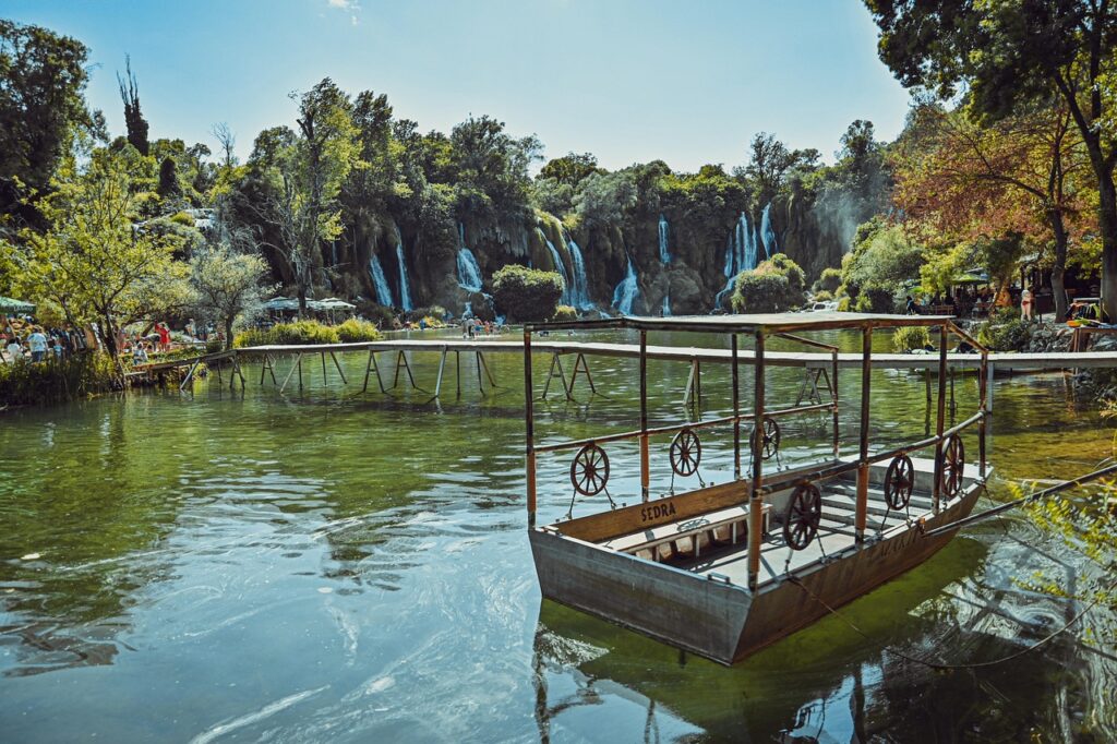 Petit bateau flottant sur des eaux calmes et turquoise, avec les chutes de Kravica en arrière-plan.