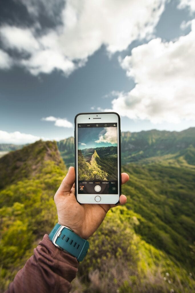 Randonnée en montagne avec smartphone Une personne capture des paysages de montagnes pittoresques avec son smartphone lors d’une randonnée en journée, entourée de sommets et de vallées sous un ciel clair, elle est connecté.