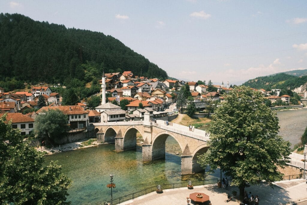 Une vue pittoresque du pont historique de Konjic s’étendant sur la rivière Neretva en Bosnie, entouré d’une végétation luxuriante et d’architecture traditionnelle.